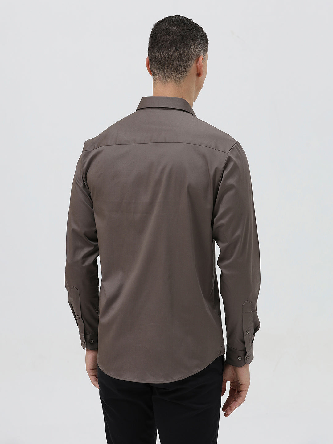 A man wearing a long-sleeve button-down dress shirt in a dark taupe-brown color, paired with black trousers, photographed against a light gray studio background.