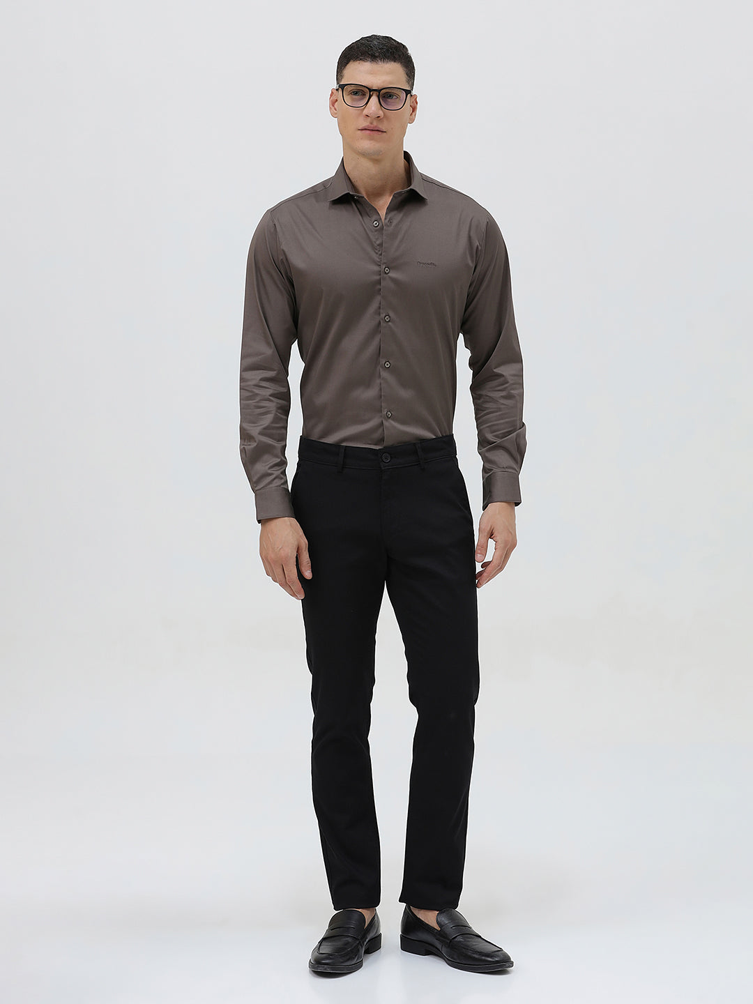 A man wearing a long-sleeve button-down dress shirt in a dark taupe-brown color, paired with black trousers, photographed against a light gray studio background.