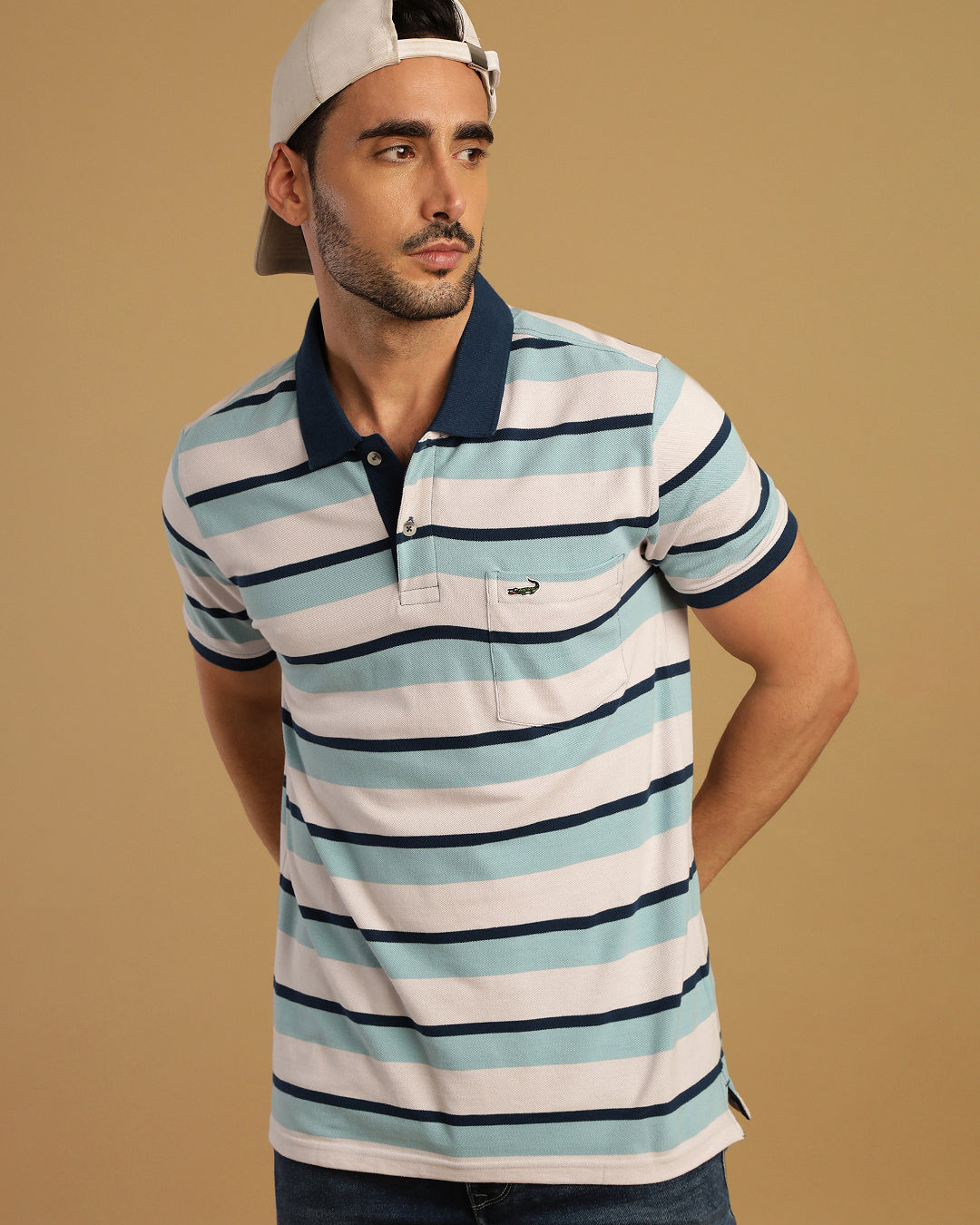 Man wearing a white blue and white striped polo t shirt with casual styling on a gray background