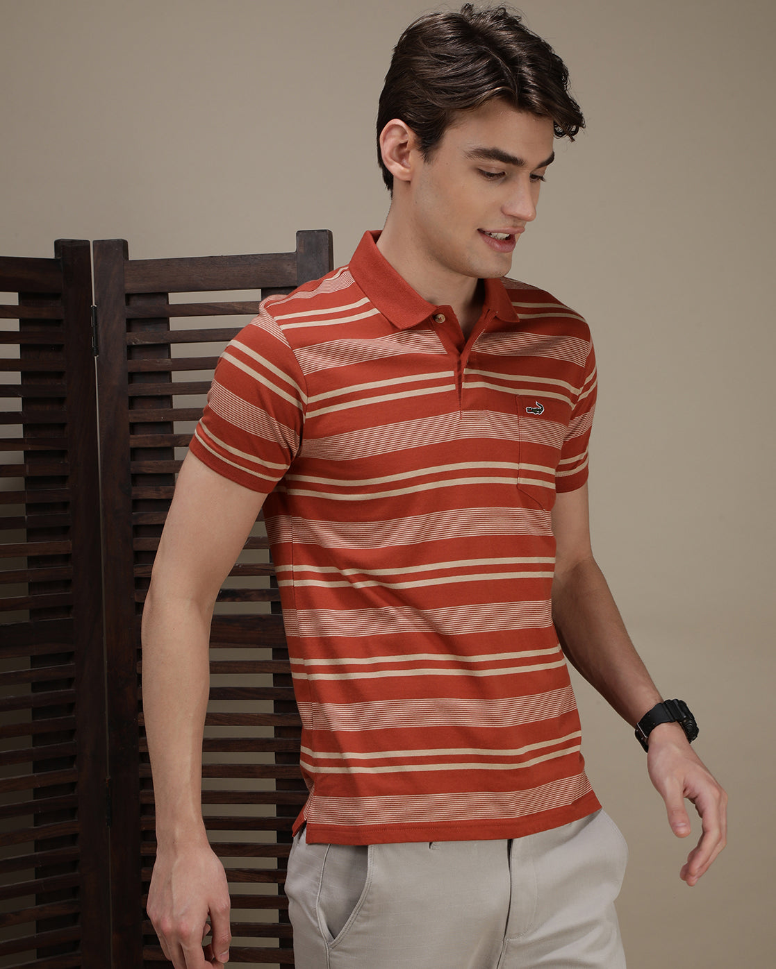 Man wearing a dusty orange striped polo t shirt with casual styling on a gray background