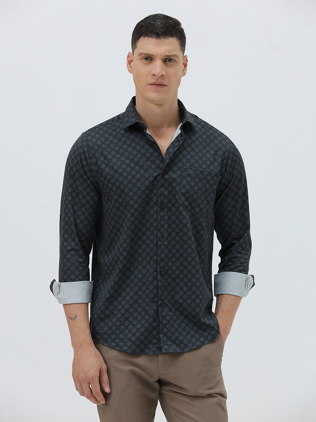 A man wearing a dark navy long-sleeve button-up shirt with a small geometric pattern and rolled-up sleeves, paired with khaki pants, against a plain light gray background.