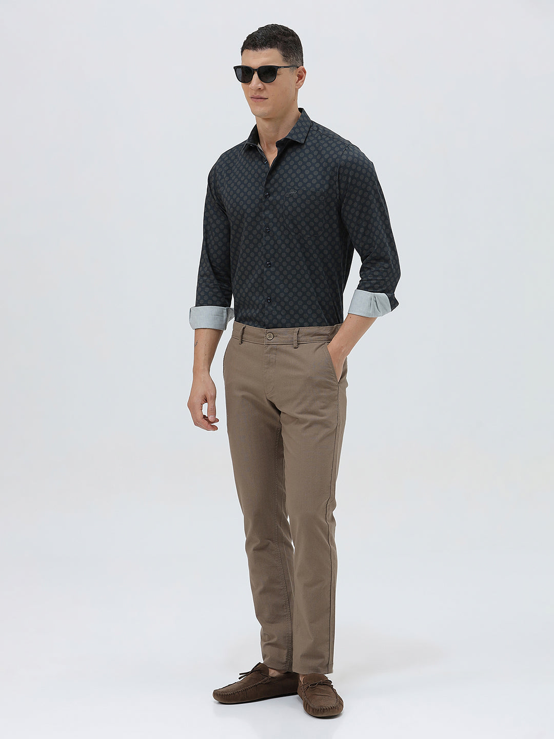 A man wearing a dark navy long-sleeve button-up shirt with a small geometric pattern and rolled-up sleeves, paired with khaki pants, against a plain light gray background.