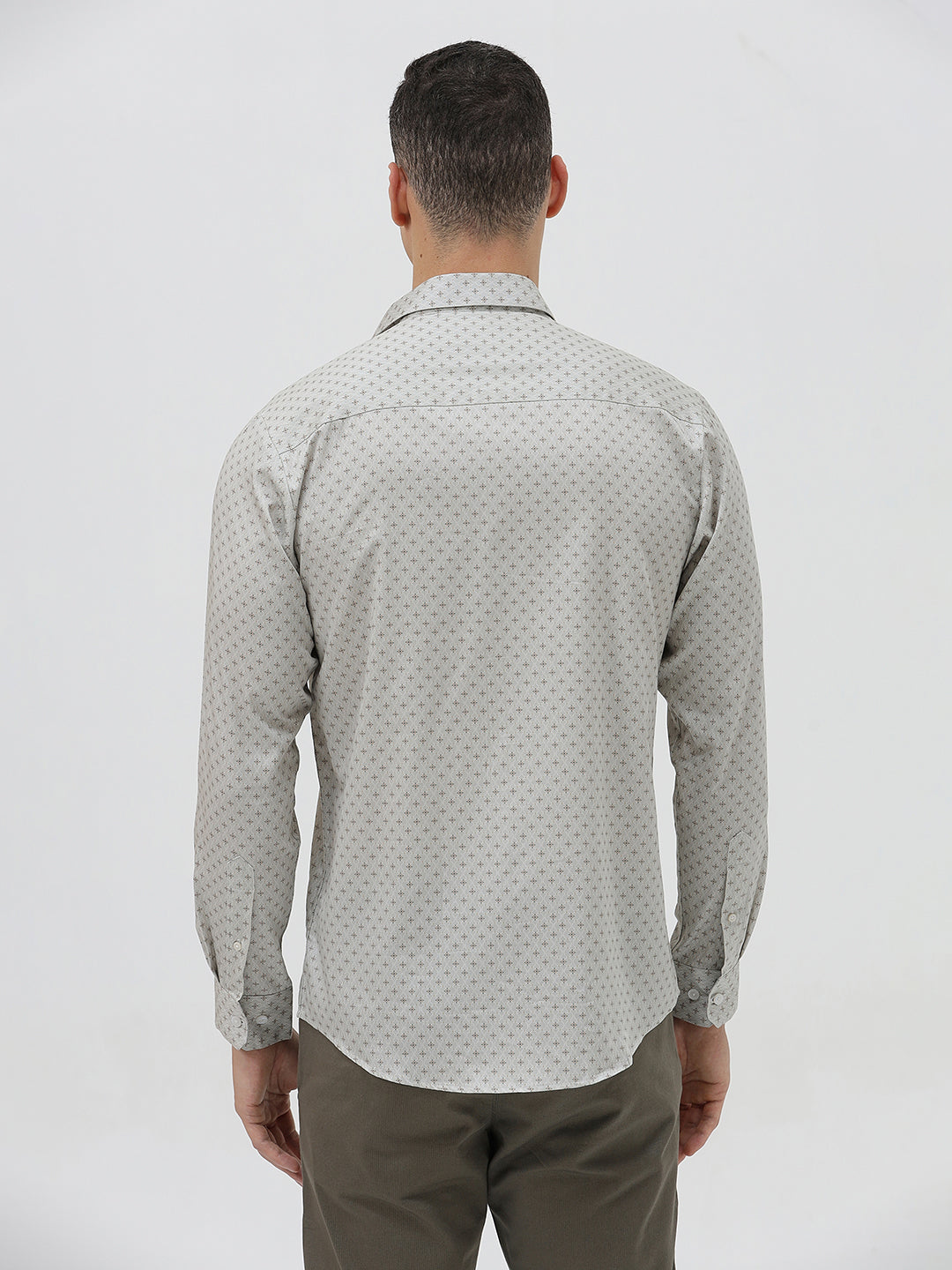 A man wearing a light gray long-sleeve button-down shirt with a small repeating geometric pattern, paired with olive green trousers, against a plain light gray background.
