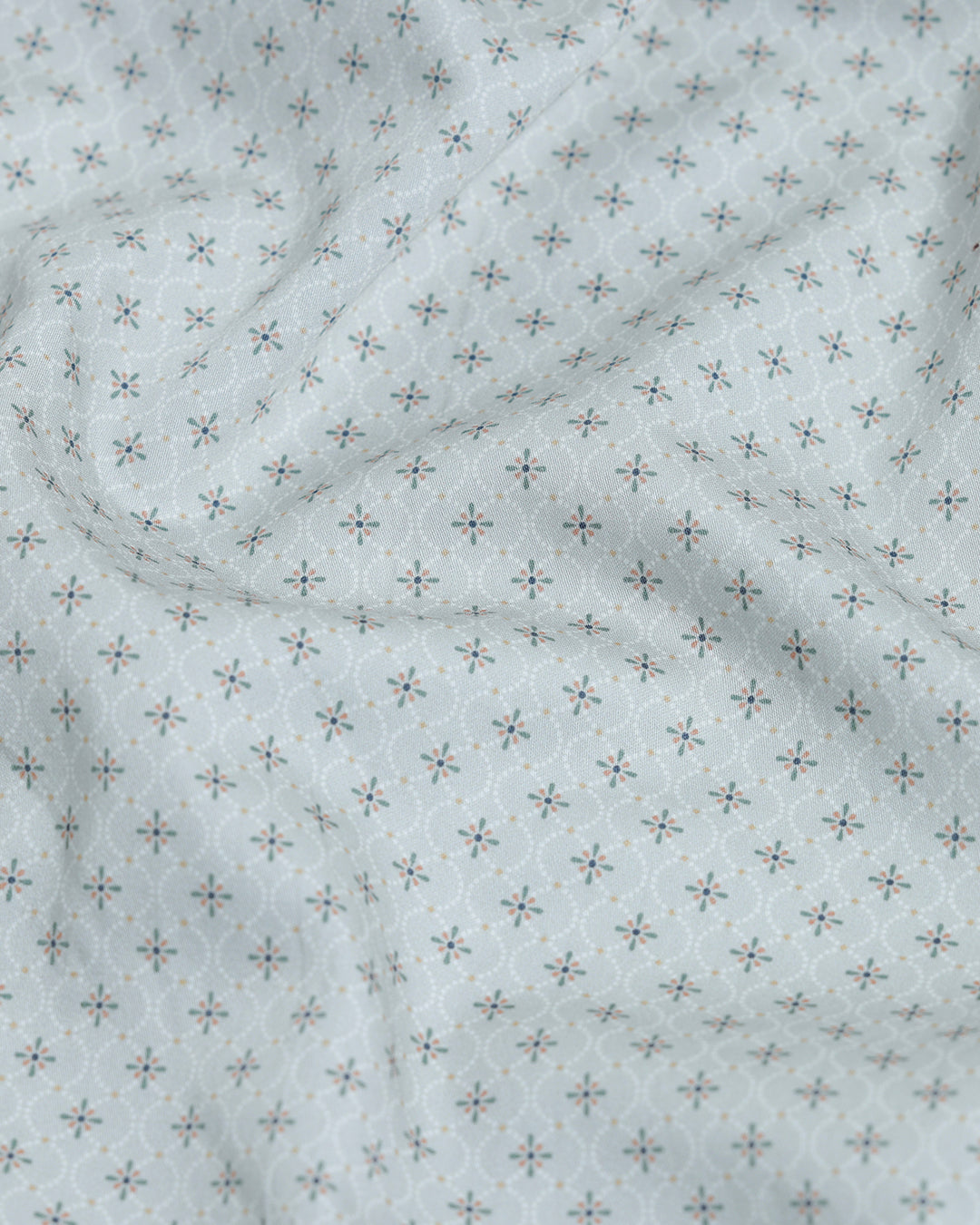 A man wearing a light gray long-sleeve button-down shirt with a small repeating geometric pattern, paired with olive green trousers, against a plain light gray background.