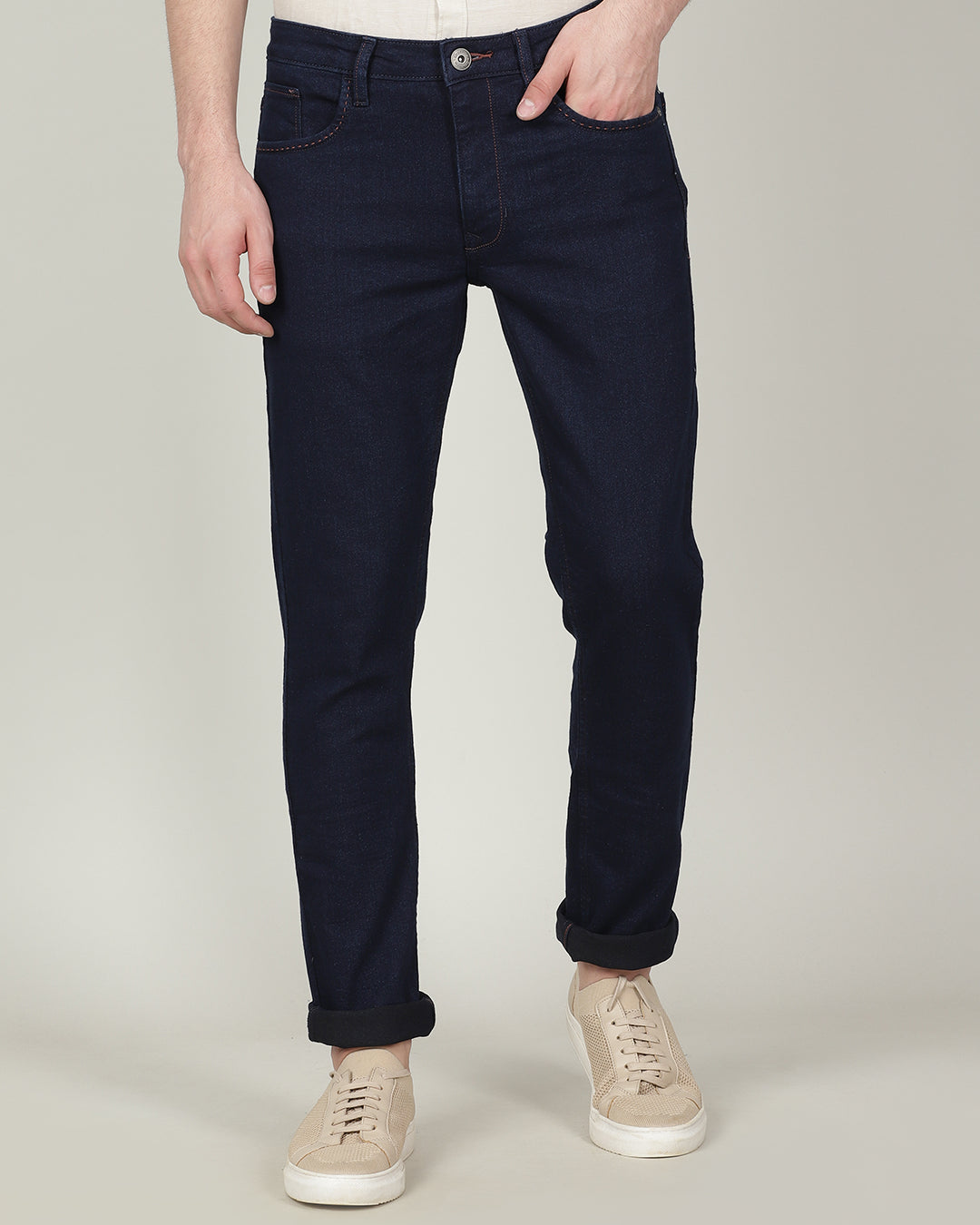 Man wearing a blue dark blue solid mid rise slim tapered jean on a light gray background
