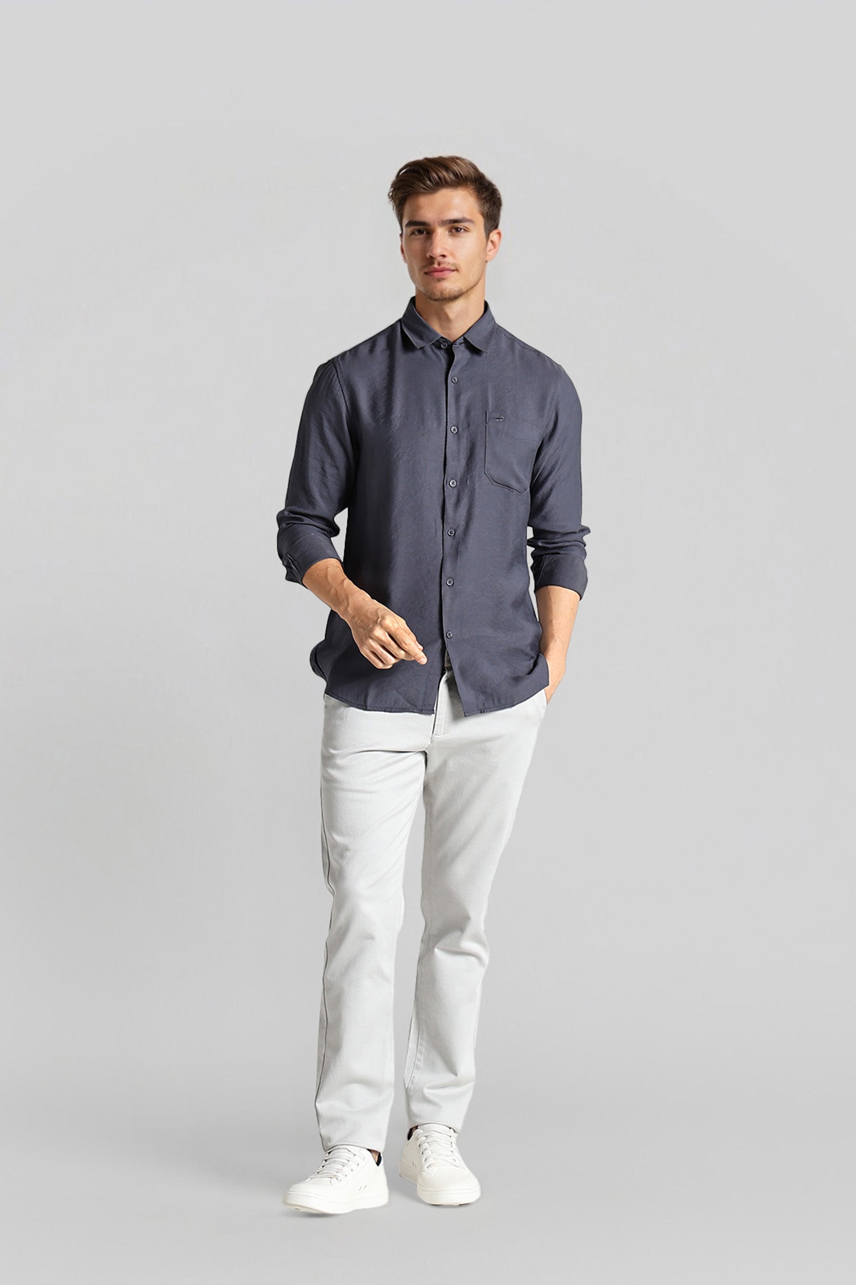 Man wearing a dark blue button-up shirt and white pants on a gray background