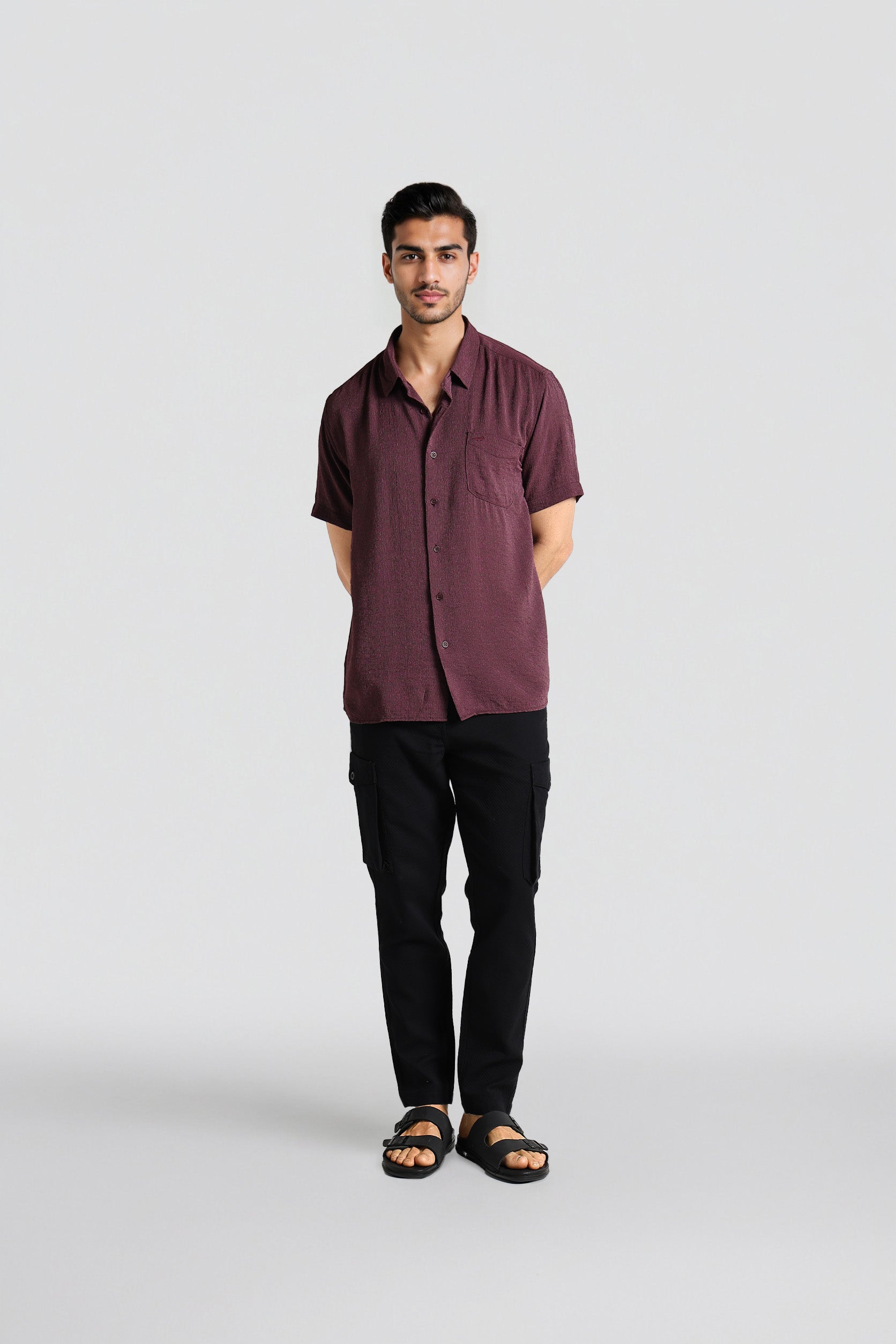 Man wearing a maroon shirt and black pants on a white background