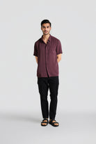 Man wearing a maroon shirt and black pants on a white background