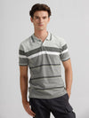 Man wearing a green slim fit green striper polo t shirt on a light gray background