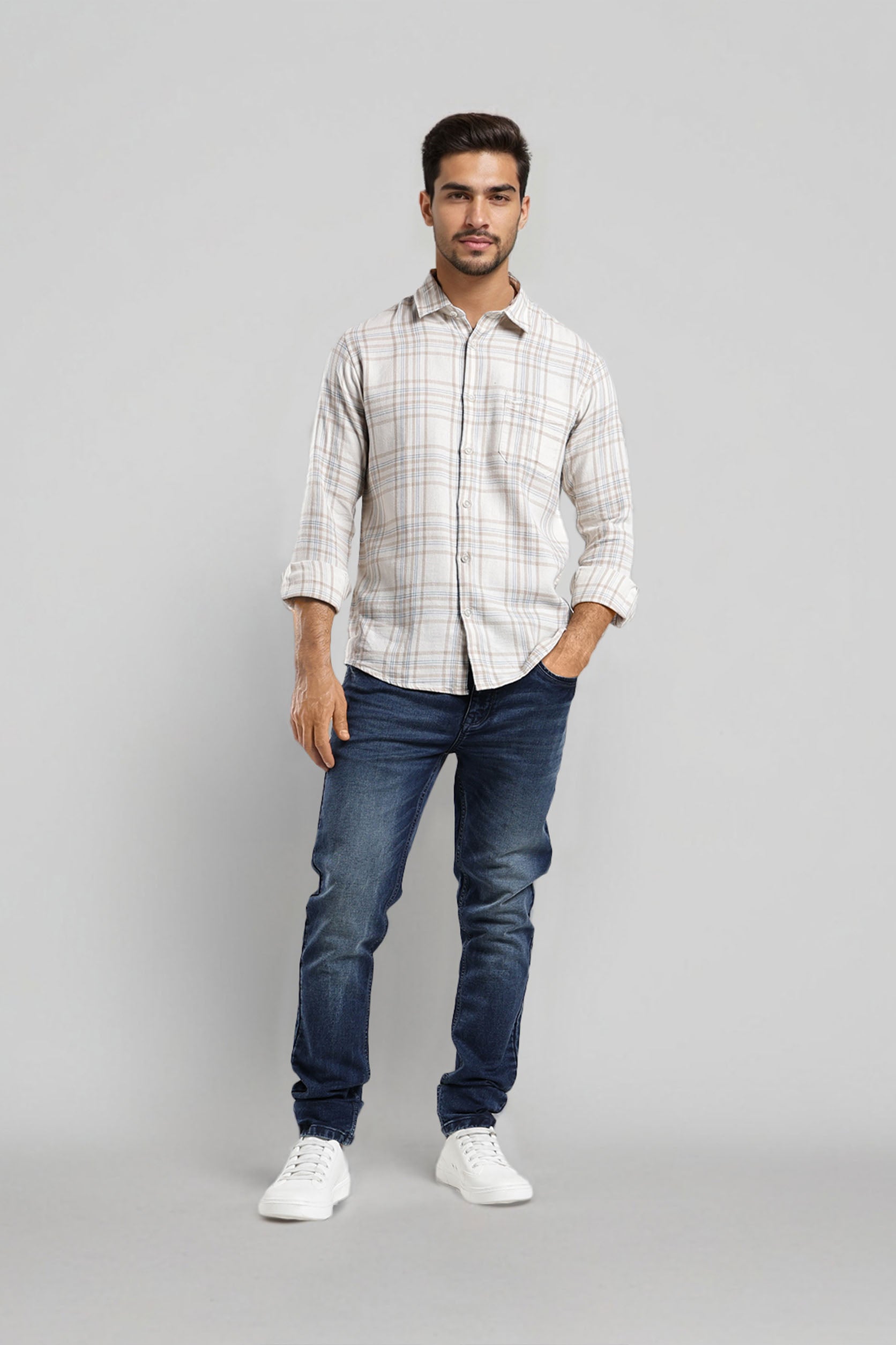 Man wearing a checkered shirt, blue jeans, and white sneakers on a gray background