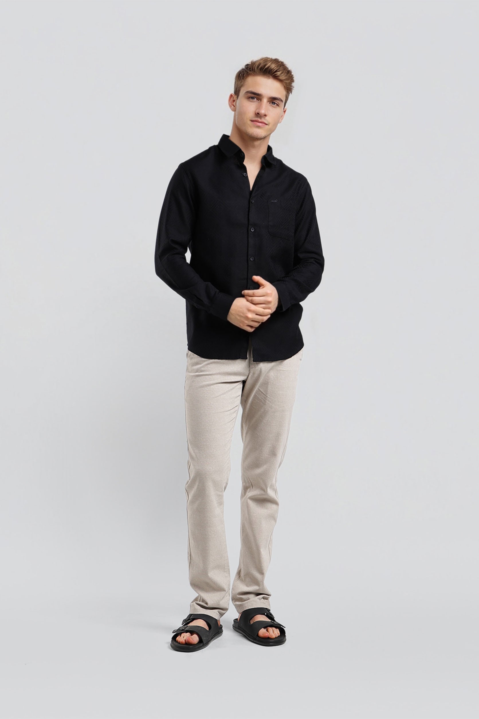 Man wearing a black shirt and beige pants on a light gray background