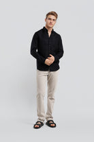 Man wearing a black shirt and beige pants on a light gray background