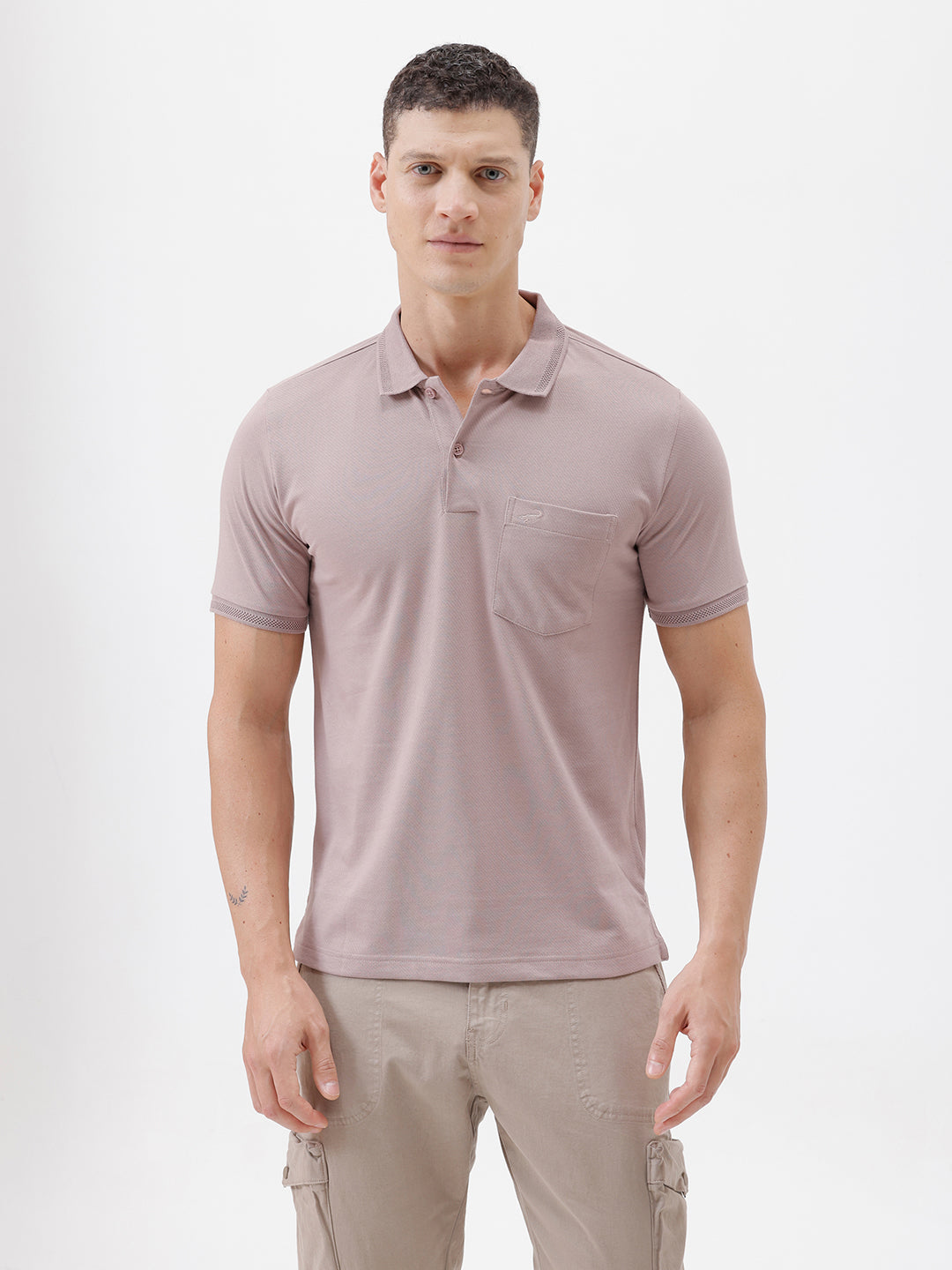 A man modeling a short-sleeve polo shirt in a dusty mauve-pink color, paired with khaki cargo pants and a baseball cap, against a plain light gray background.