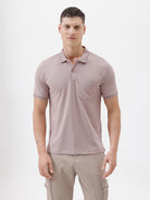 A man modeling a short-sleeve polo shirt in a dusty mauve-pink color, paired with khaki cargo pants and a baseball cap, against a plain light gray background.