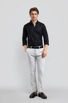 Man wearing a black shirt, white pants, and black shoes on a light gray background