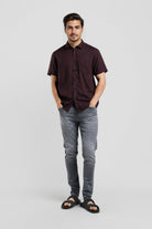 Man wearing a dark brown shirt and gray pants on a light gray background