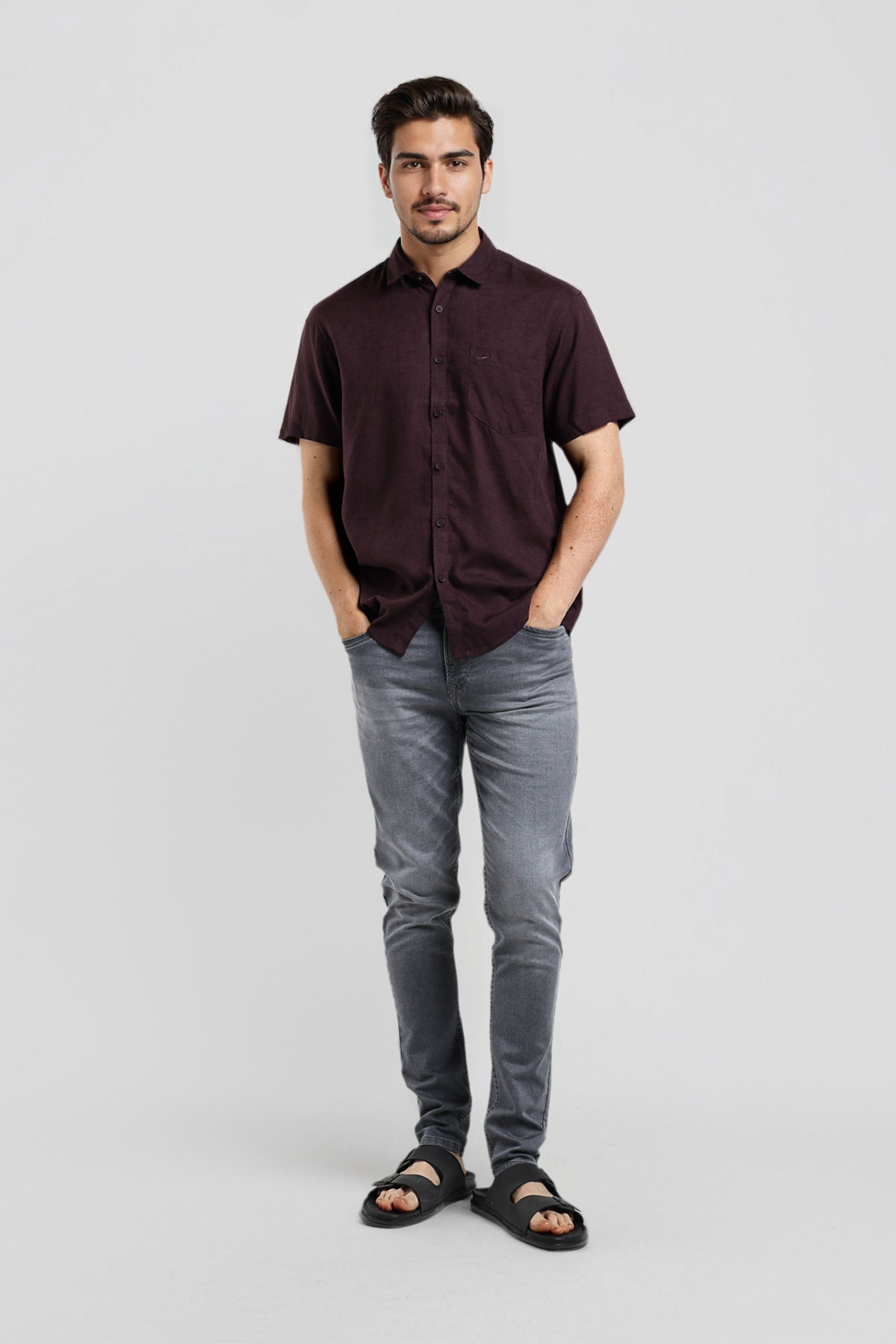 Man wearing a dark brown shirt and gray pants on a light gray background