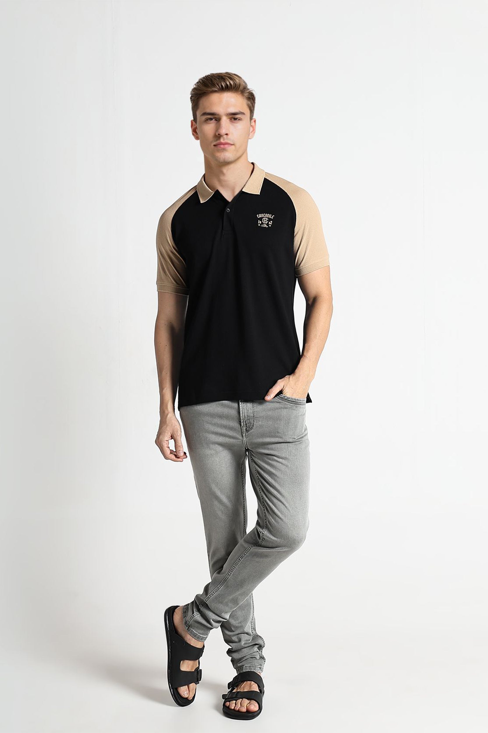 Man wearing a black and beige polo shirt with gray pants on a white background