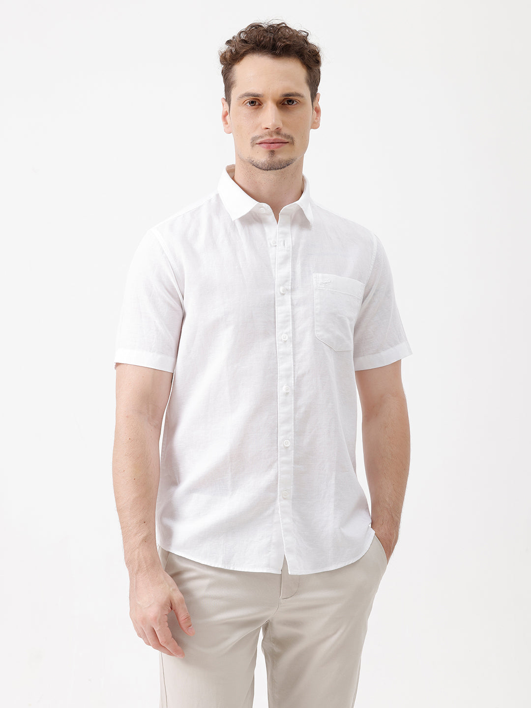 A man wearing a white short-sleeve button-up shirt with a chest pocket and beige trousers, standing against a plain white studio background.