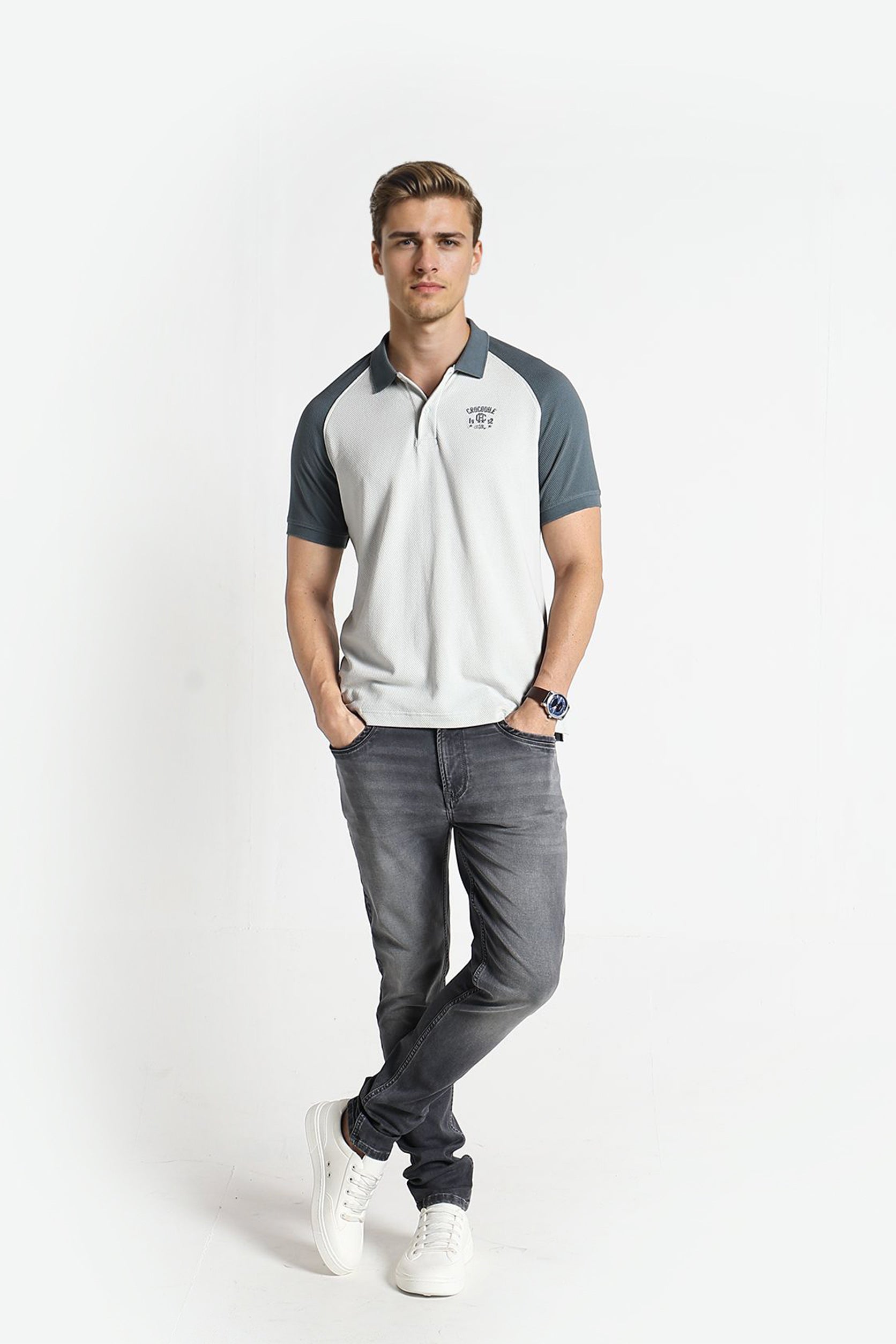 Man wearing a white and gray polo shirt with dark gray pants on a white background