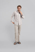 Man wearing a light gray shirt and beige pants against a gray background