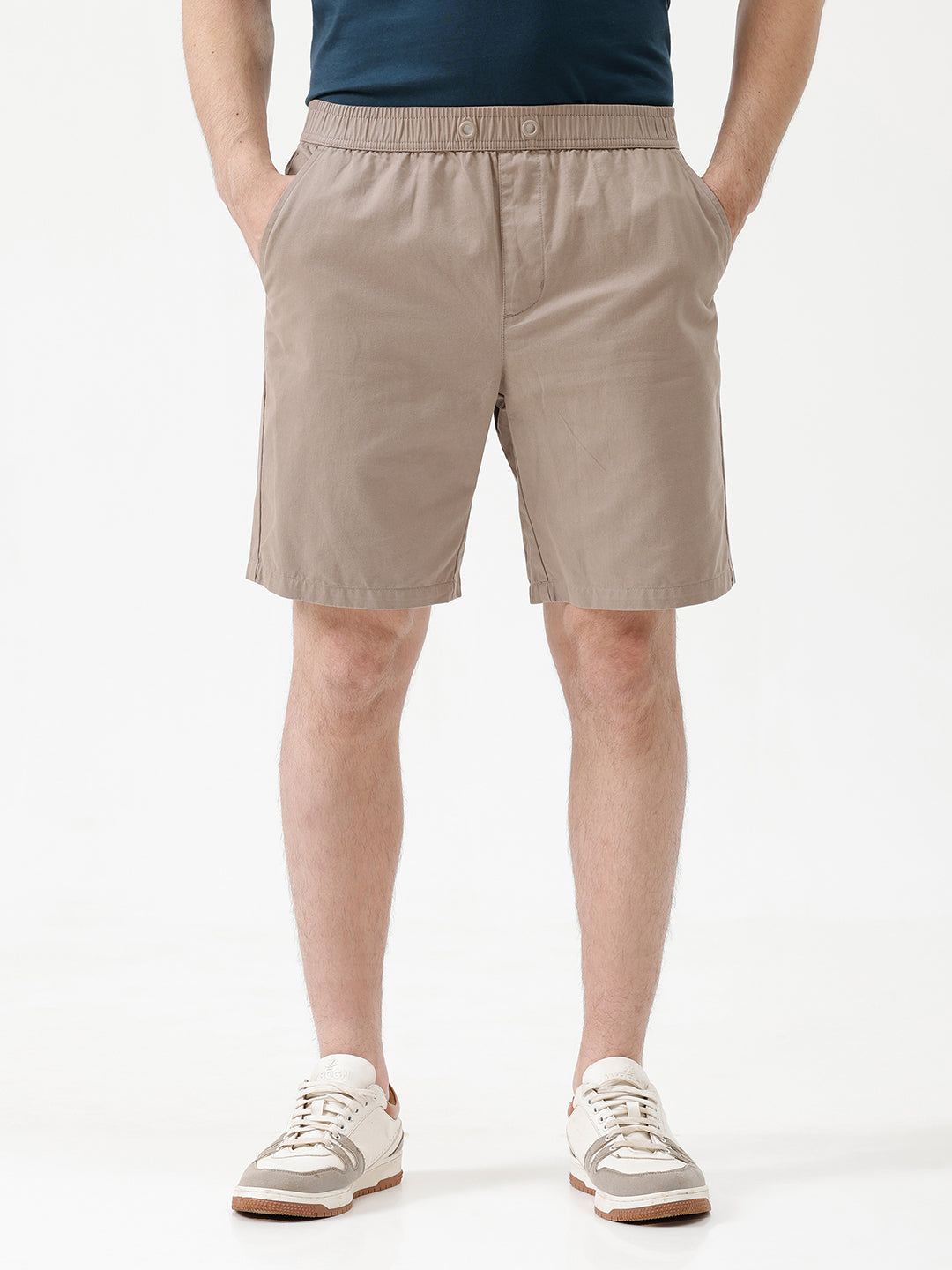 A person wearing beige drawstring shorts, a navy blue t-shirt, and white sneakers, shown from the waist down against a plain white studio background.