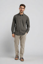 Man wearing a dark gray button-up shirt and beige pants on a light gray background