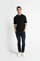 Man wearing a black t-shirt and dark jeans on a white background