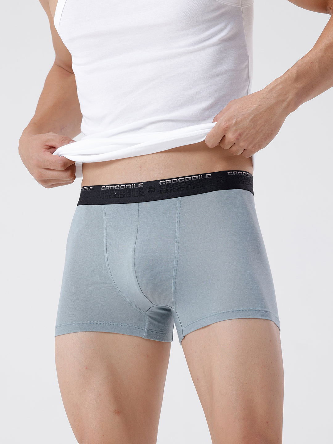 Person wearing light gray boxer briefs with a white shirt on a plain background