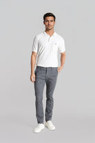 Man wearing a white polo shirt and gray pants on a gray background