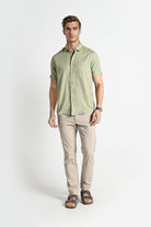 Man wearing a light green short-sleeve shirt and beige pants on a white background