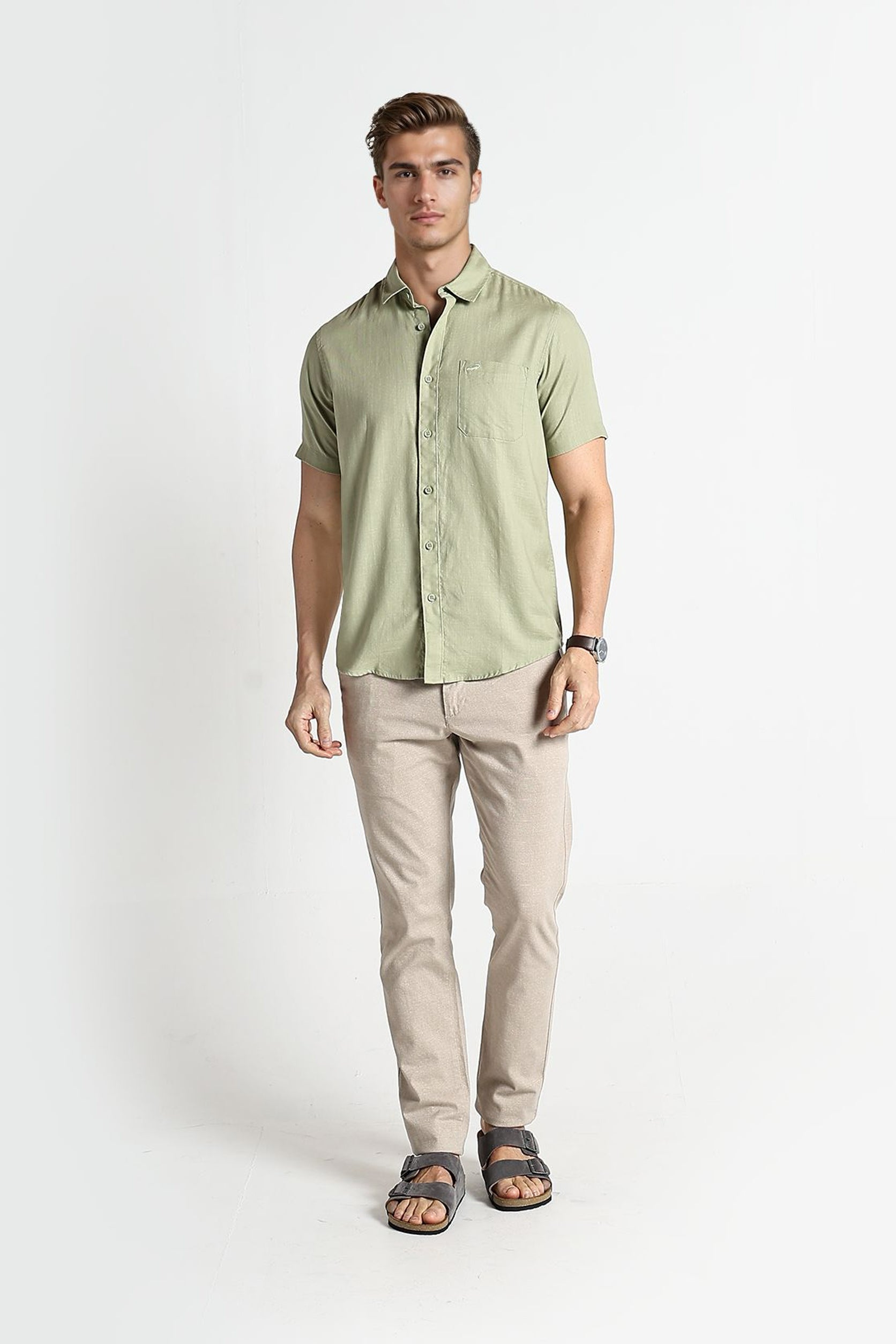 Man wearing a light green short-sleeve shirt and beige pants on a white background