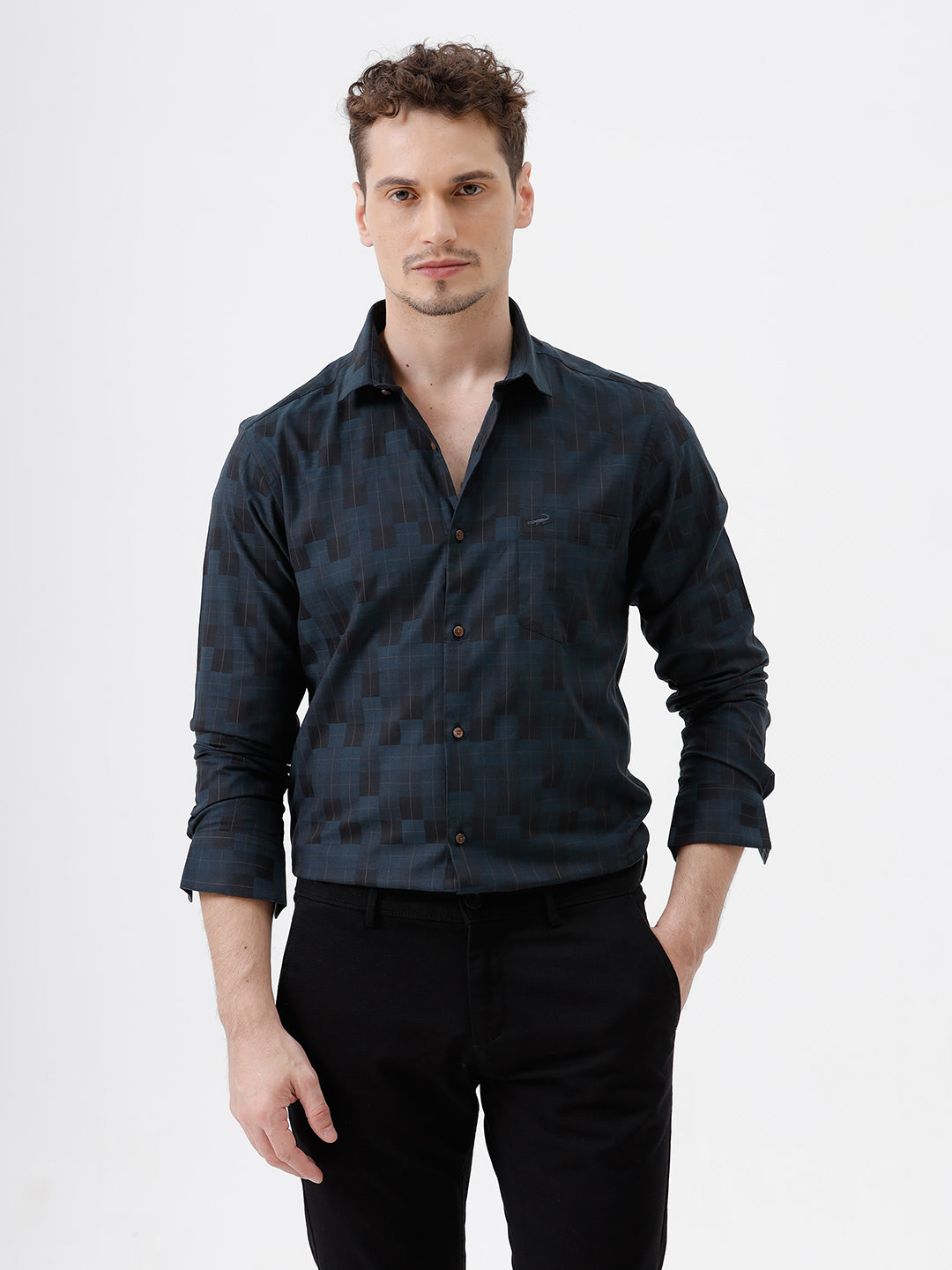 A man wearing a dark navy blue patterned long-sleeve button-up shirt and black trousers, standing against a plain white studio background.