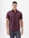 A man modeling a short-sleeve button-up shirt in a deep plum purple color, paired with gray trousers, against a plain white studio background.