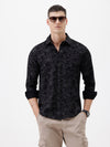 A man wearing a black long-sleeve button-up shirt with a subtle tonal floral pattern, paired with beige cargo pants and dark sunglasses, standing against a plain white background.