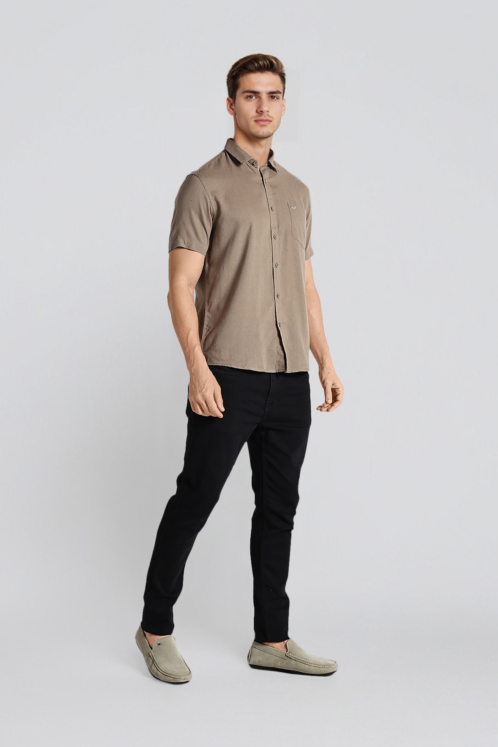 Man wearing a beige short-sleeve shirt and black pants on a white background