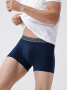 Person wearing navy blue boxer briefs with a white shirt on a light gray background