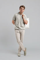 Man wearing a striped polo shirt and beige pants holding a white bag on a gray background