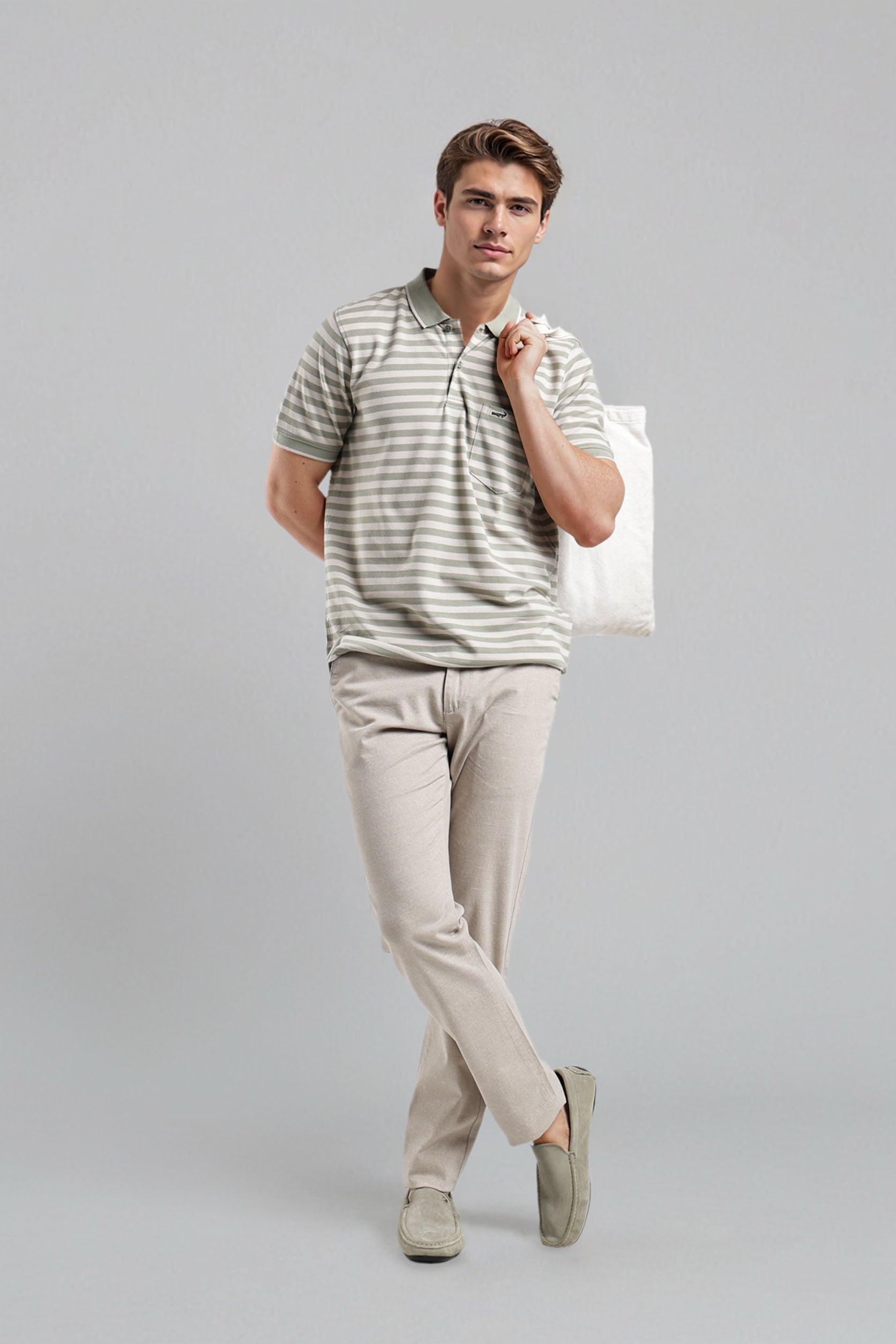 Man wearing a striped polo shirt and beige pants holding a white bag on a gray background