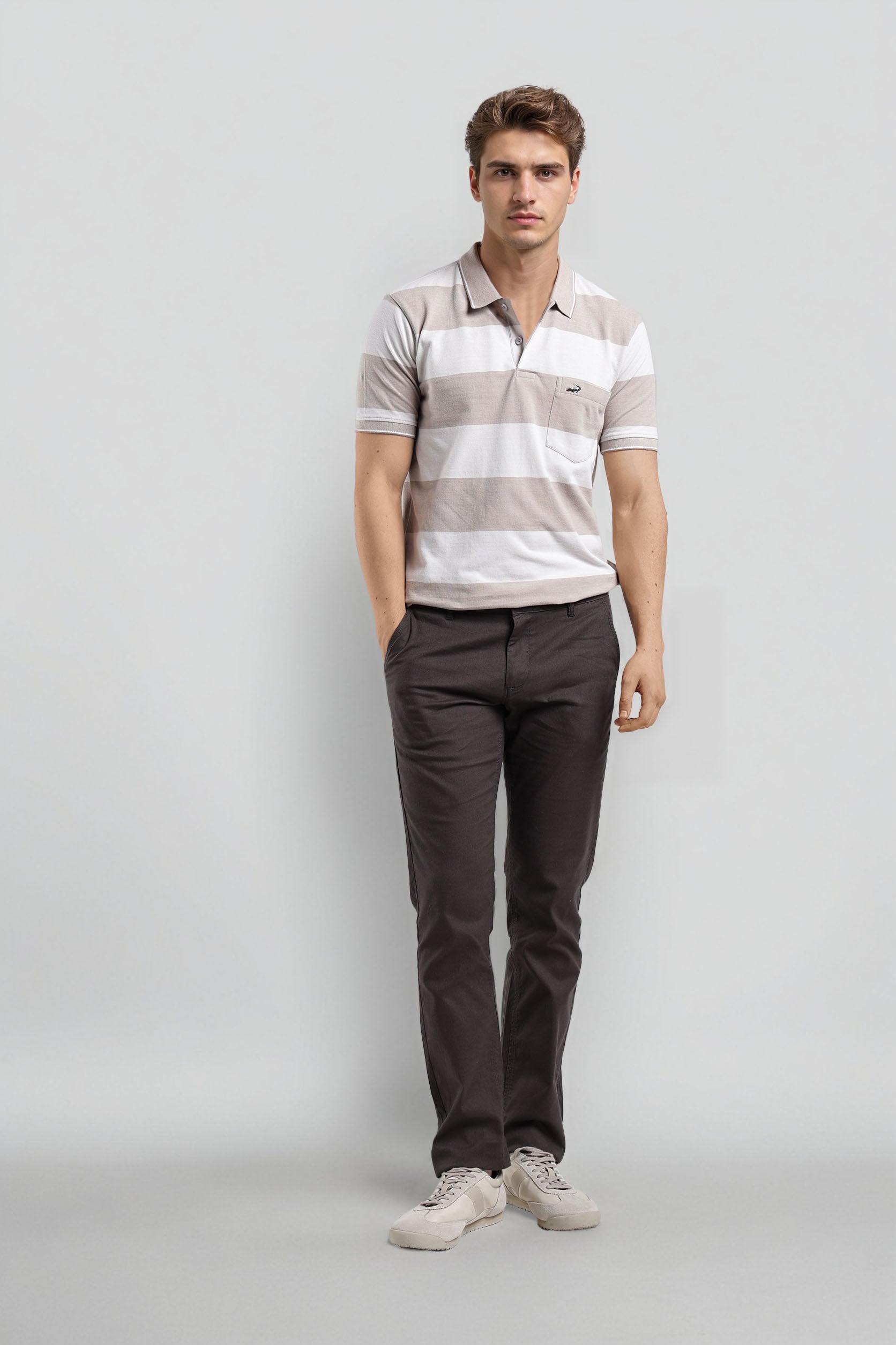 Man wearing a striped polo shirt and dark pants on a gray background