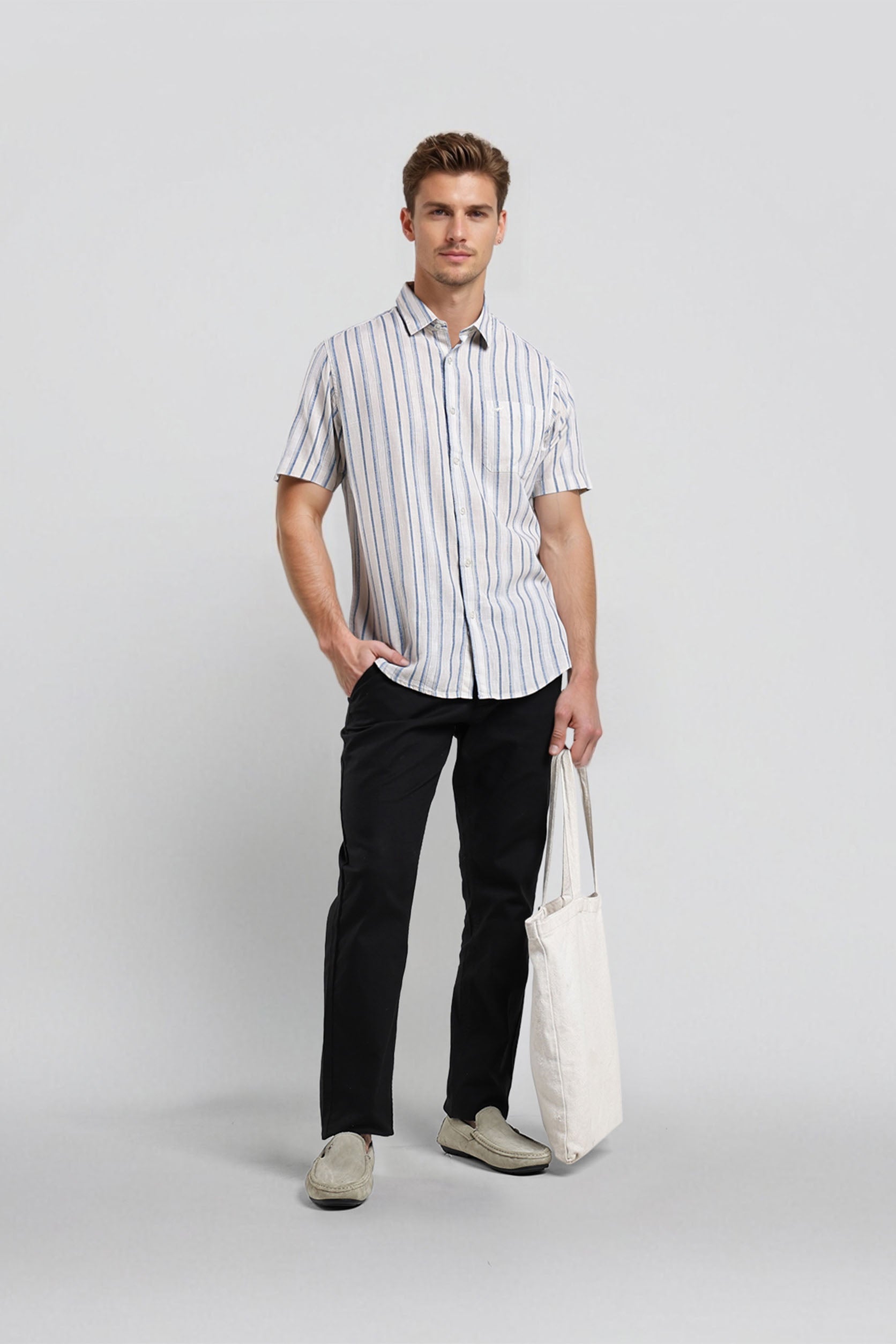 Man wearing a striped shirt and black pants holding a white bag on a light gray background