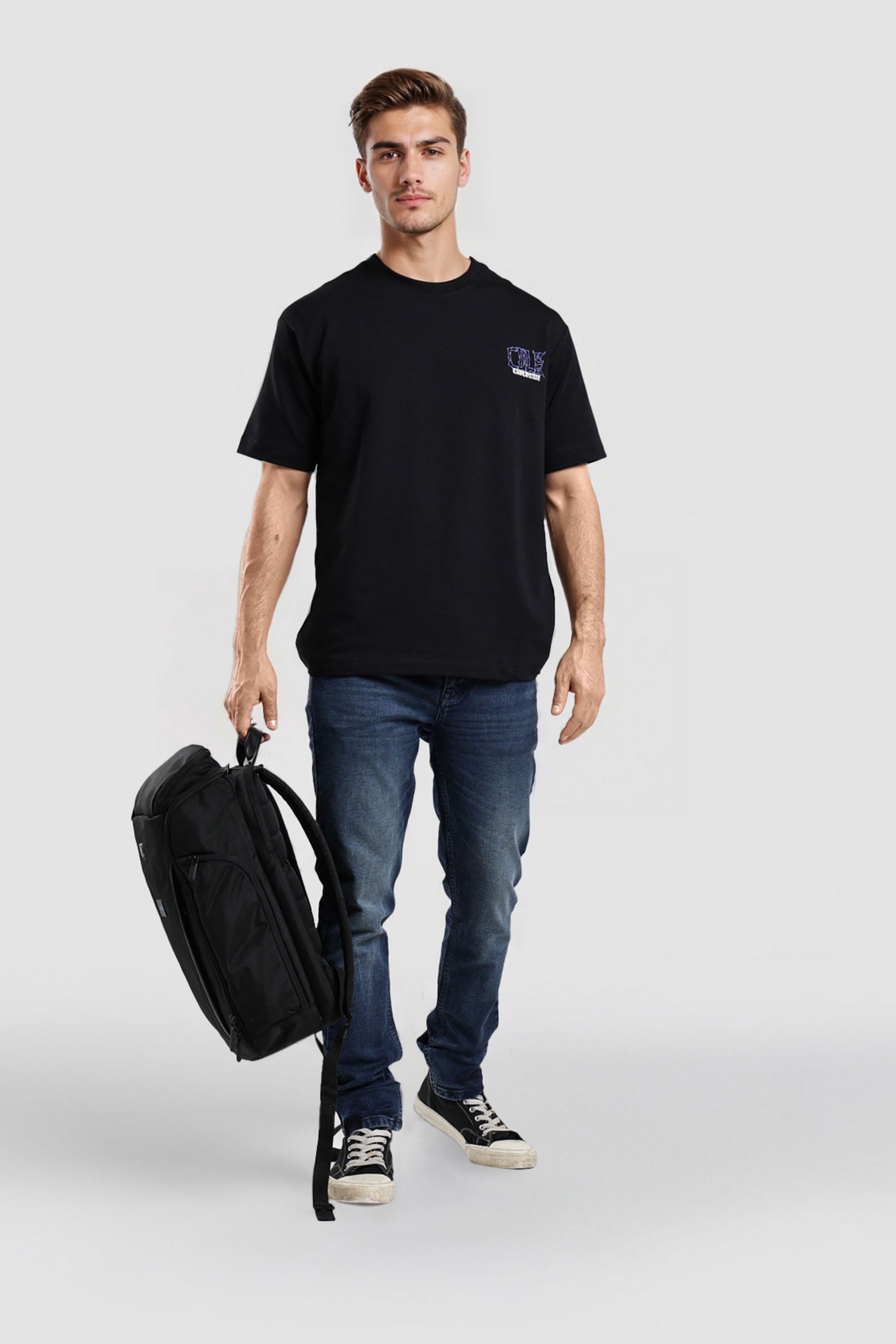 Man holding a black backpack wearing a black t-shirt and blue jeans on a white background