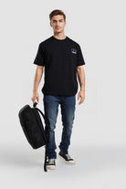 Man holding a black backpack wearing a black t-shirt and blue jeans on a white background
