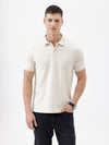 A man wearing a short-sleeve polo shirt in cream with subtle horizontal textured stripes, paired with dark jeans, standing against a plain white studio background.