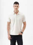 A man wearing a short-sleeve polo shirt in cream with subtle horizontal textured stripes, paired with dark jeans, standing against a plain white studio background.