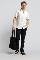 Man wearing a white shirt and black pants holding a black bag on a gray background