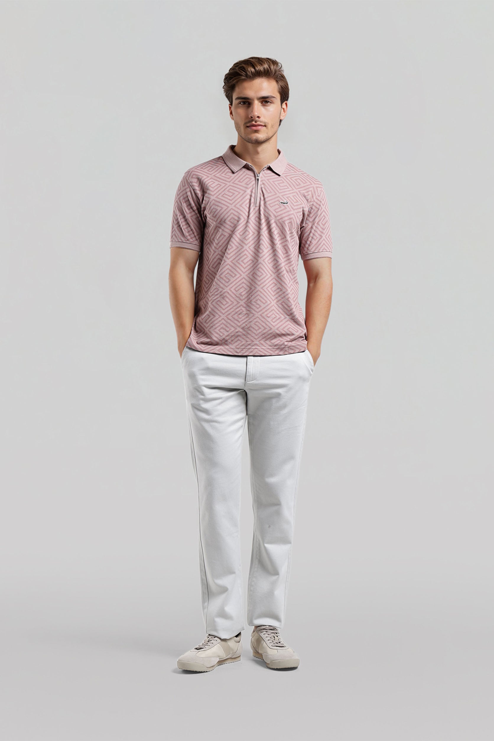 Man wearing a pink patterned polo shirt and white pants on a gray background