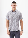 A man wearing a short-sleeve button-up shirt with a gray and white abstract pattern, paired with dark gray trousers, standing against a plain white studio background.