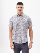 A man wearing a short-sleeve button-up shirt with a gray and white abstract pattern, paired with dark gray trousers, standing against a plain white studio background.