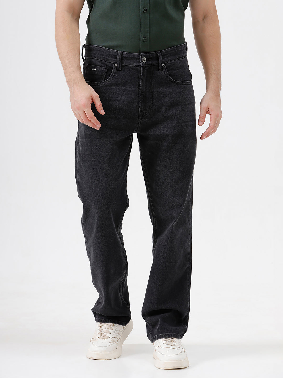 A person wearing dark washed denim jeans, a dark green shirt, and white sneakers, shown from the chest down against a plain light gray studio background.